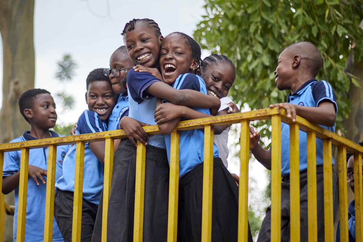 Bomas Academy students laughing and hugging on the playground railing
